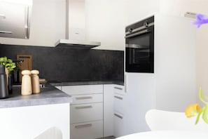 Une cuisine moderne avec des meubles blancs, un plan de travail noir et un four encastré.