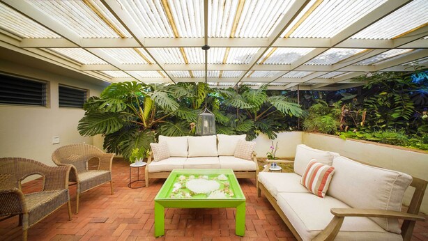 An indoor patio with a white sofa, wicker chairs, a green coffee table, and lush tropical plants. - 4 Mi to Beach! Ocean-view Group Haven in Honolulu (Honolulu)
