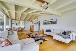 A spacious living area with a white sofa, a wooden dining table with chairs, a white couch, and a large rug.