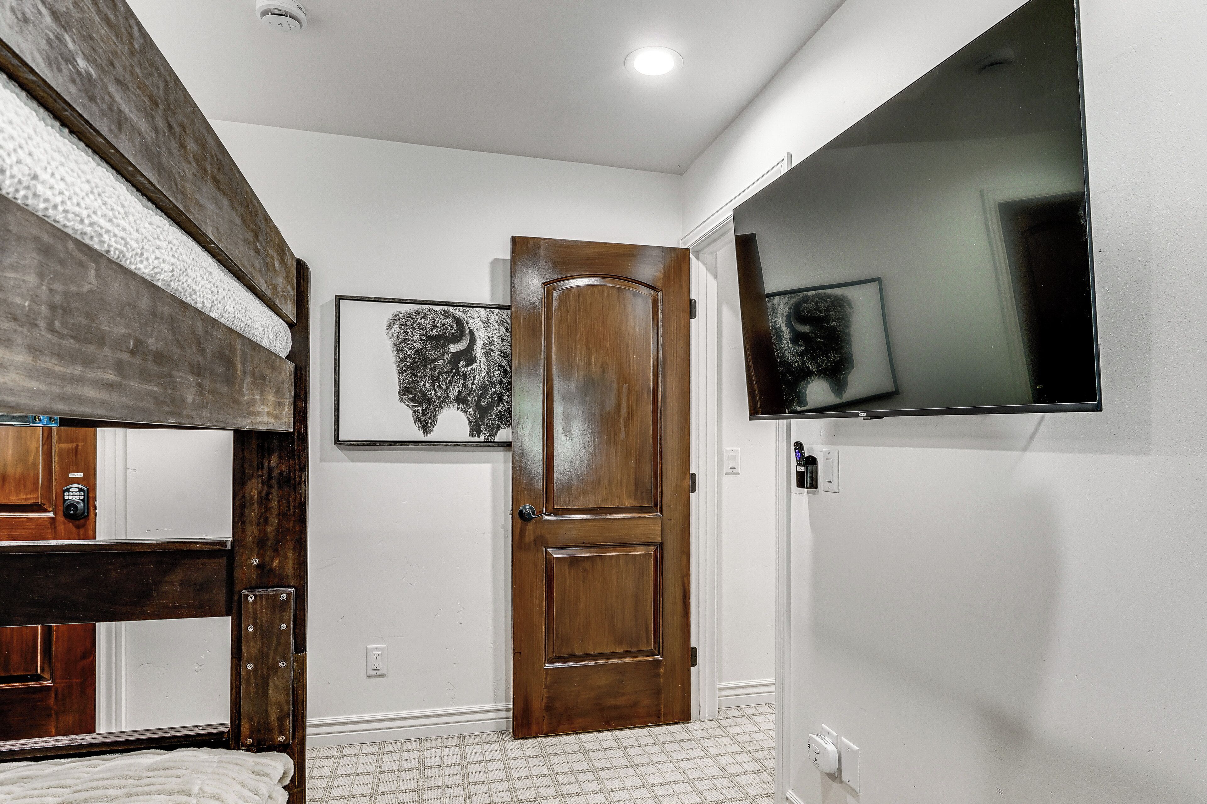 A room with a bunk bed, a wooden door, a framed picture, and a mounted TV.
