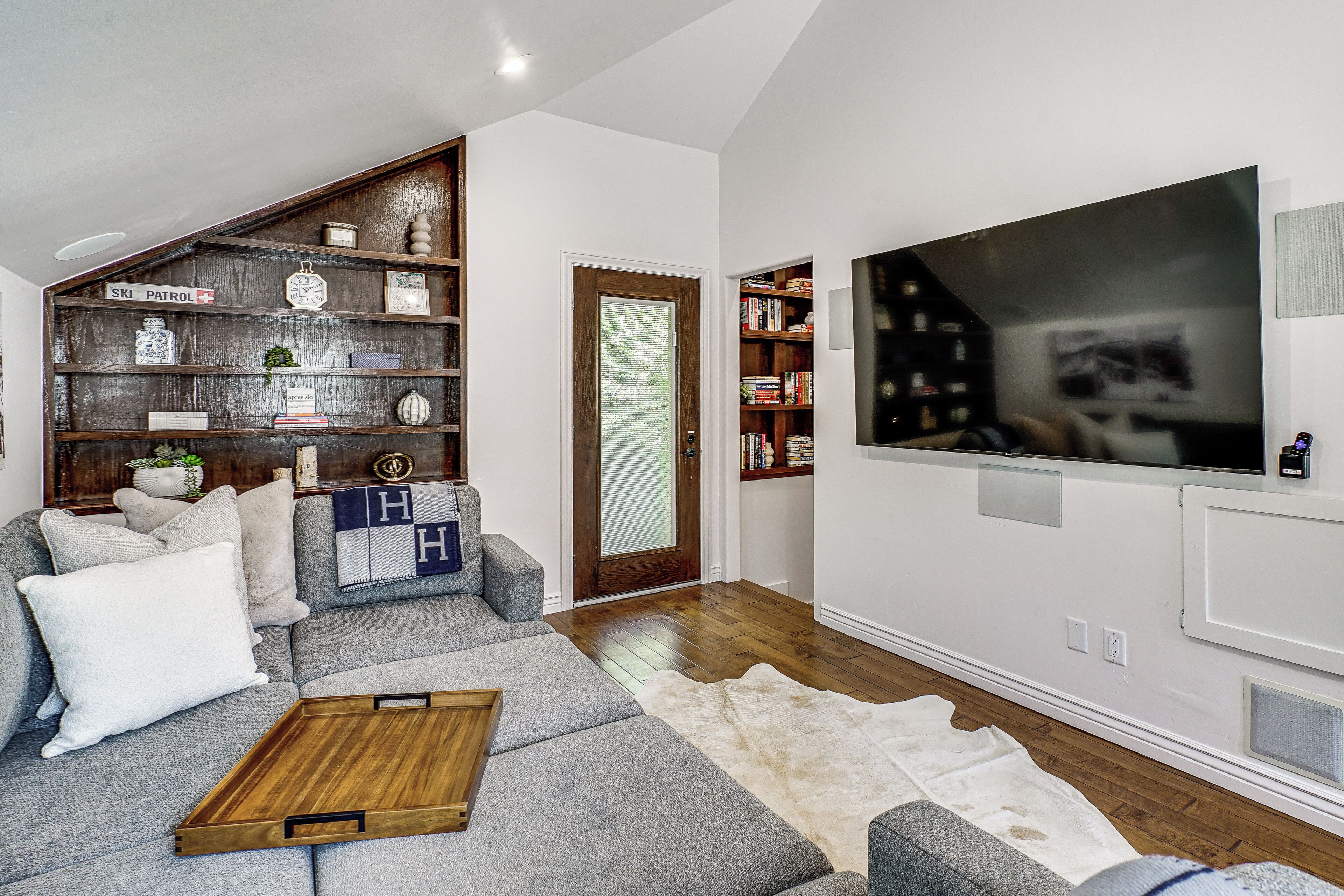 Una sala de estar con un sofá modular, una mesa de centro de madera, un televisor de pantalla plana grande y una estantería.