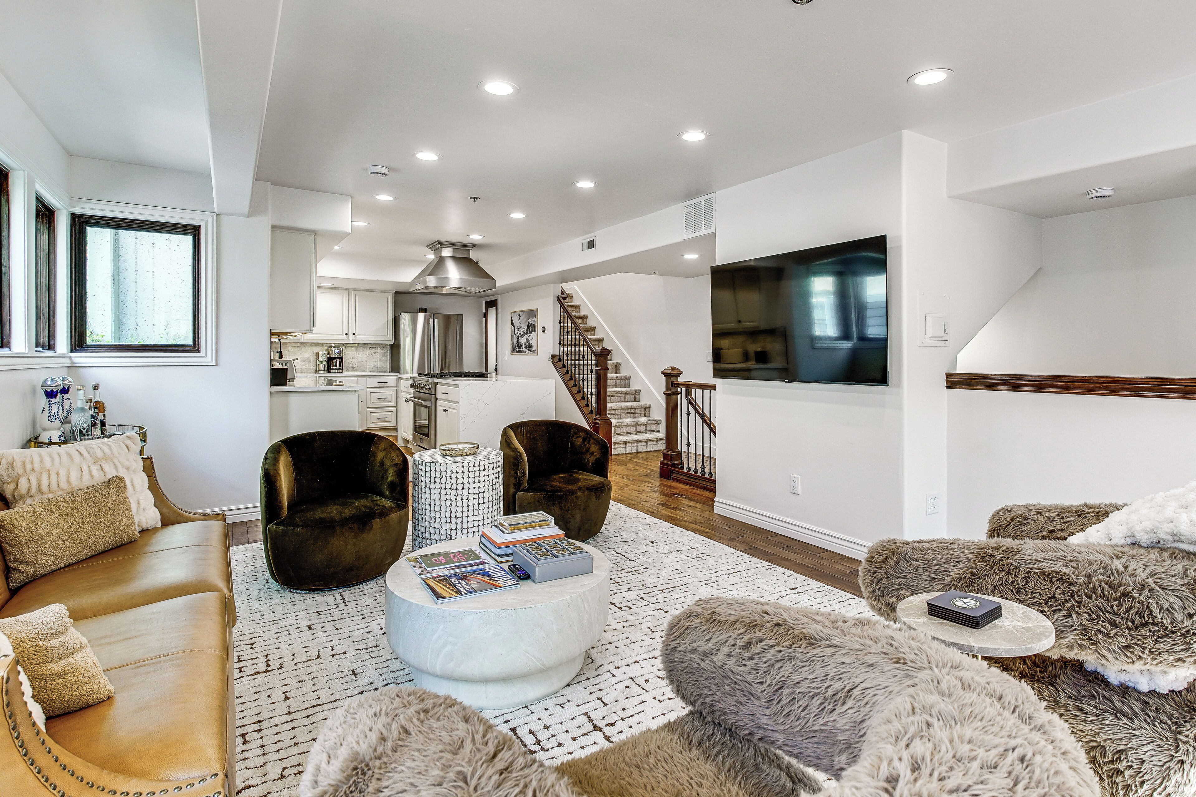 A modern living room with a sofa, armchairs, a coffee table, and a staircase leading to a kitchen.