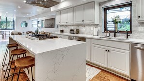 A modern kitchen with white cabinets, a marble island, bar stools, and a large window. - Park City Gem w/ Hot Tub + Sauna: Walk to Main St (Park City)