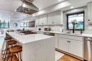 A modern kitchen with white cabinets, a marble island, bar stools, and a large window. - Park City Gem w/ Hot Tub + Sauna: Walk to Main St (Park City)