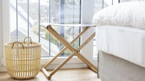 Um quarto com cama, janela com vista, piso de madeira e cesta de vime.