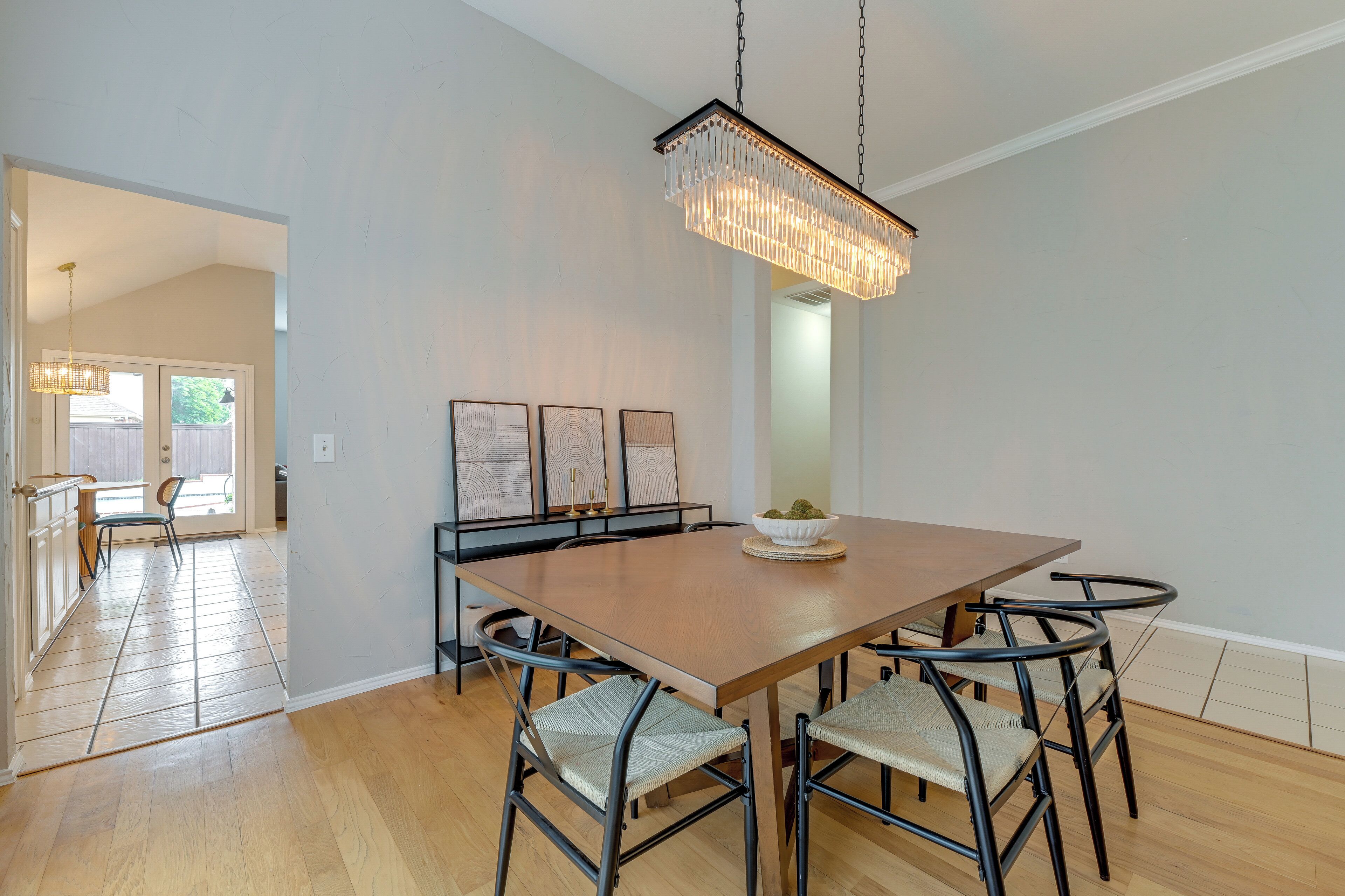 Un comedor con una mesa de madera, sillas de metal negro, una lámpara de araña y cuadros en la pared.