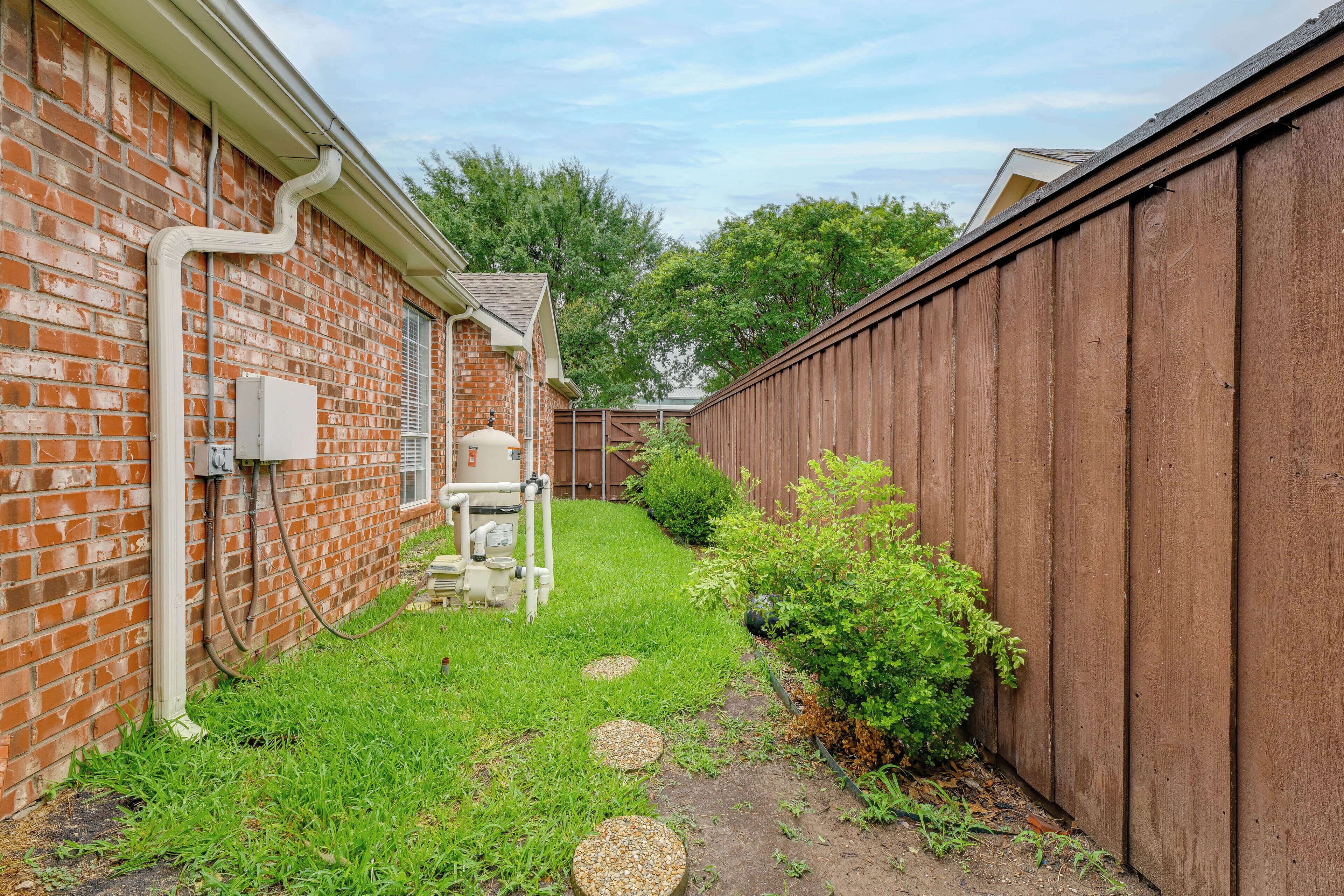 A backyard with a brick wall, a wooden fence, and a small garden area with stepping stones.