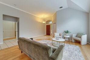 A modern living room with a sofa, coffee table, and armchairs. There is a door leading to another room and a small side table with a plant.