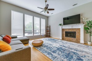 Ein Wohnzimmer mit einer Couch, einem runden Holzhocker, einem Kamin und einem darüber montierten Fernseher.