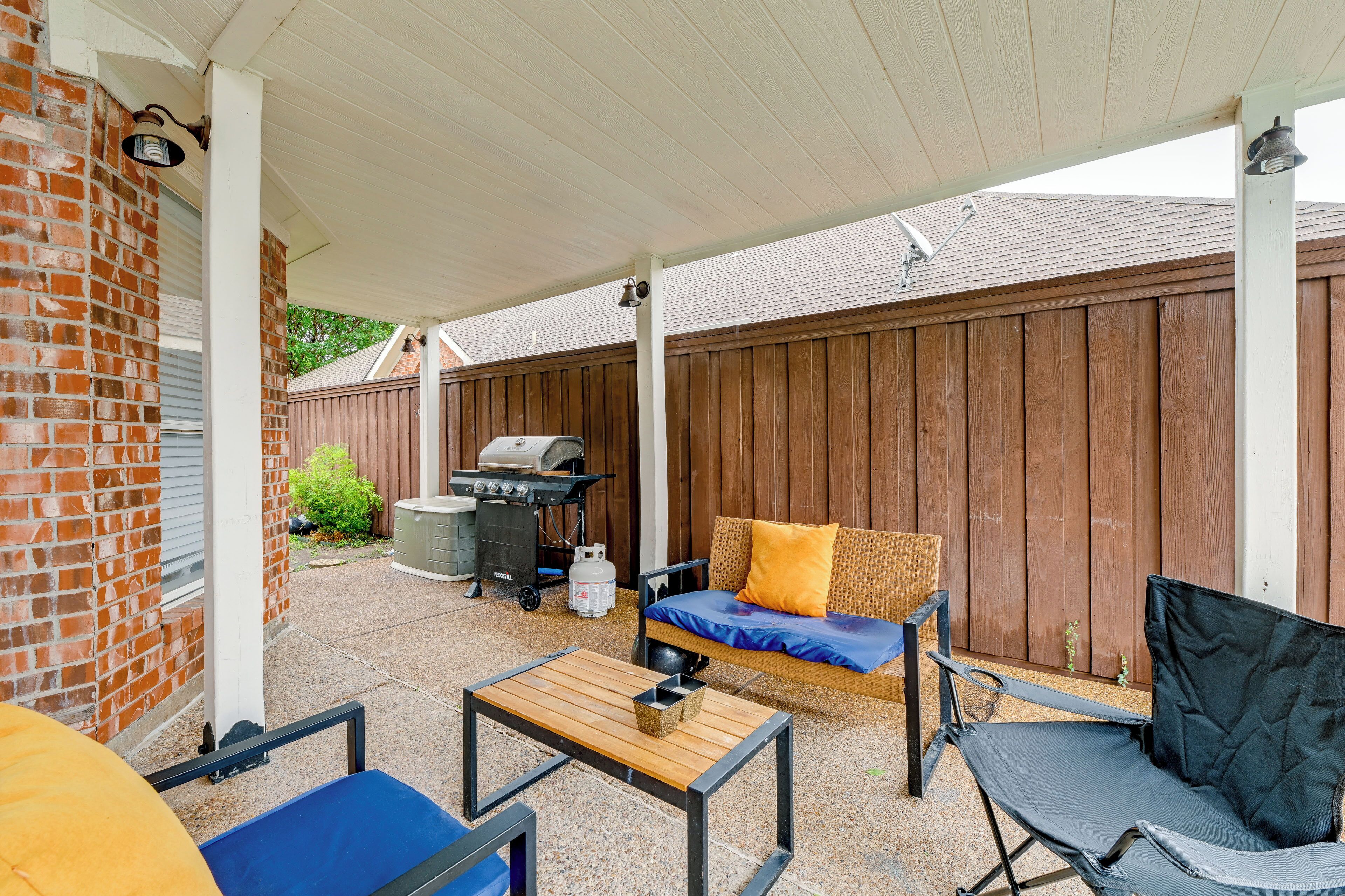A covered patio area with a brick wall, a wooden fence, a grill, and outdoor furniture.