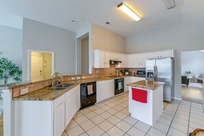 A modern kitchen with white cabinetry, granite countertops, a stainless steel refrigerator, and a dishwasher.