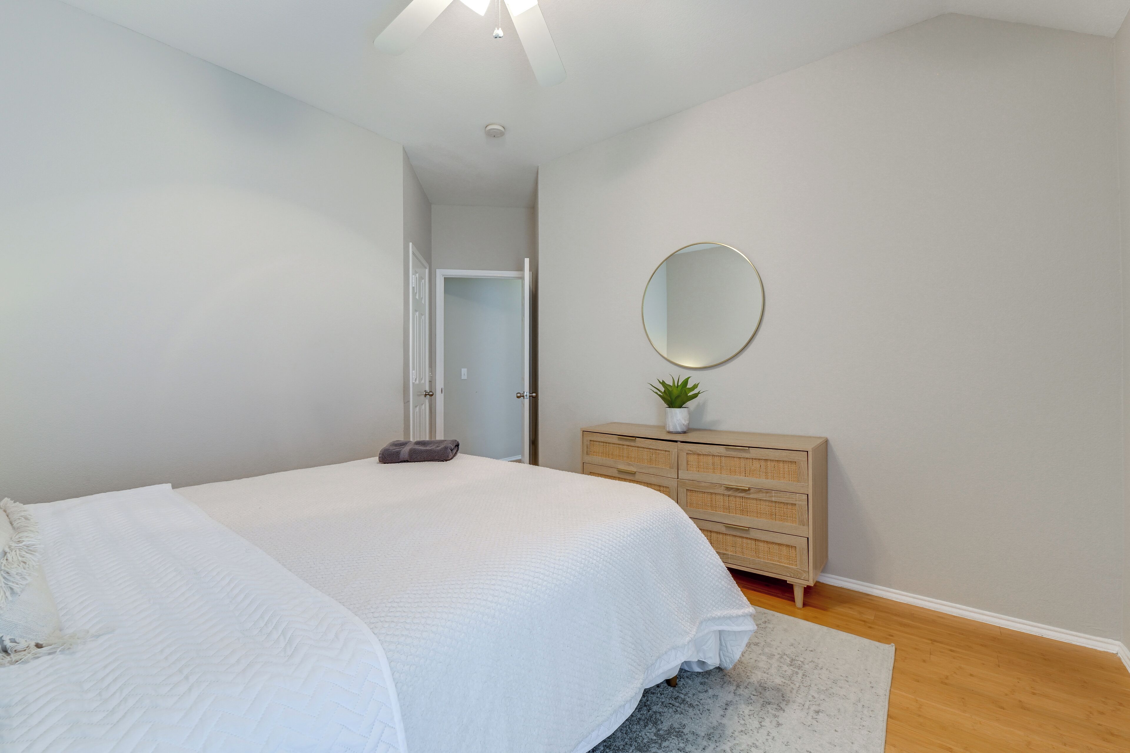 A bedroom with a bed, a dresser, a mirror, and a door leading to another room.