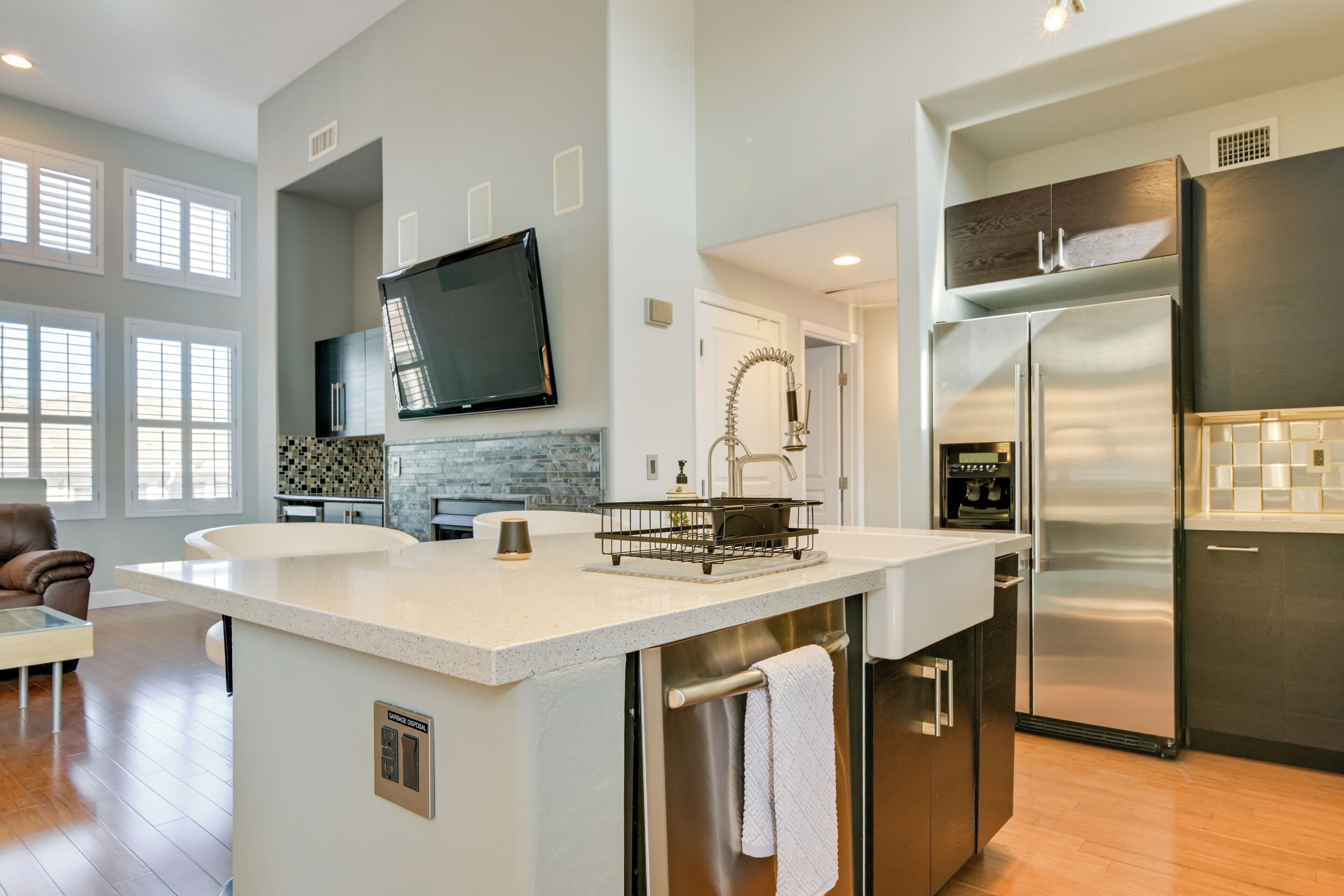 A modern kitchen with a central island, stainless steel appliances, and a flat-screen TV mounted on the wall.