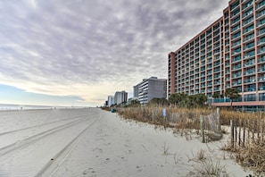 Una playa con un sendero arenoso, una valla de madera y un hotel de varios pisos con balcones.