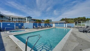 Una piscina con lettini, una zona relax a bordo vasca e un edificio dalla facciata blu.