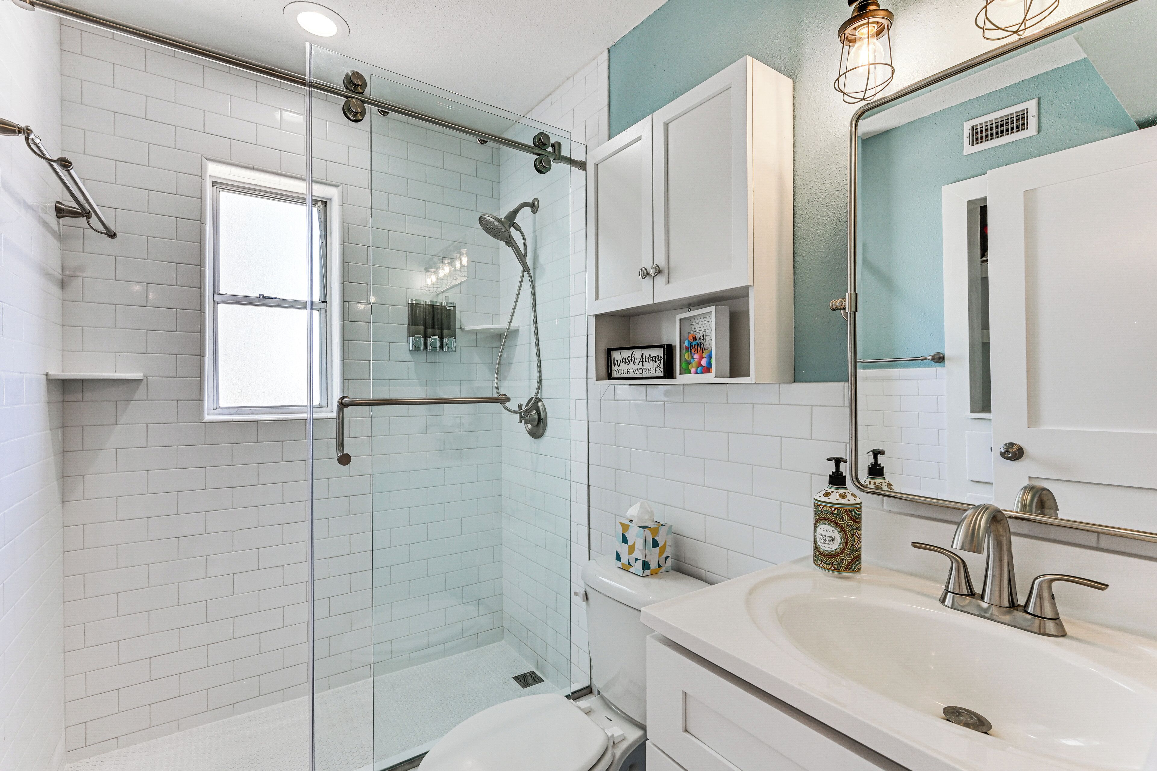 Un baño moderno con cabina de ducha de vidrio, un lavamanos blanco con un solo grifo y un espejo con luz integrada.