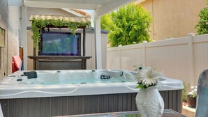 Un bain à remous avec une terrasse en bois, une clôture blanche et un arbre en arrière-plan.
