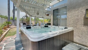 Un bain à remous installé sous une pergola, avec une terrasse en pierre et une vue sur une maison.