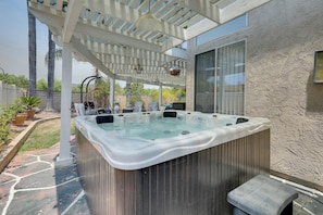 Ein Whirlpool unter einer Pergola mit einer Steinterrasse und Blick auf ein Haus.