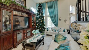 Un salon avec un grand téléviseur à écran plat, un sapin de Noël, un canapé blanc et un escalier.