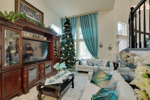 Ein Wohnzimmer mit einem großen Flachbildfernseher, einem Weihnachtsbaum, einem weißen Sofa und einer Treppe.