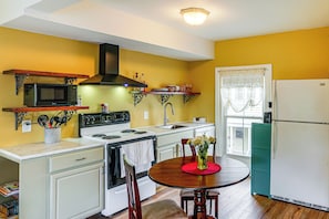 A kitchen with a stove, microwave, and refrigerator, wooden cabinets, and a dining table with chairs. - Peaceful Upstate Retreat! Walk to Hudson River (Coxsackie)