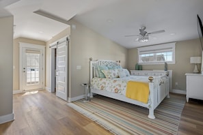 A bedroom with a bed, a ceiling fan, a window, and a door.