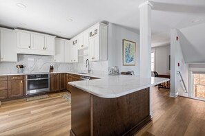 A modern kitchen with white cabinetry, a marble countertop, and a wooden floor.
