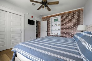 Ein Schlafzimmer mit einem Bett, einem Deckenventilator, einer Ziegelwand, einer weißen Tür und einem Regal mit Dekoration.