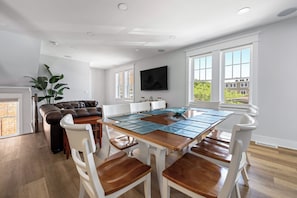 A dining area with a wooden table, white chairs, and a brown leather sofa.