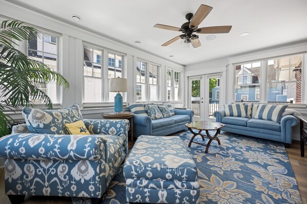 A spacious living room with a large window, a ceiling fan, and a patterned rug.