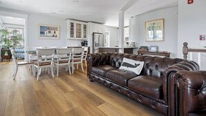 A modern living room with a brown leather sofa, white dining chairs, and a kitchen area in the background. - Downtown Lewes on 2nd Street - #104 - 2nd floor apartment (Lewes)