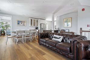 Ein modernes Wohnzimmer mit einer braunen Ledersofa, weißen Esstischen und einer Küchenzeile im Hintergrund.