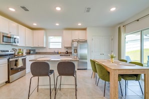 A modern kitchen with white cabinets, a stainless steel refrigerator, and a dining area with a wooden table and green chairs.
