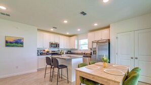 A modern kitchen with white cabinets, a central island, and a dining area with green chairs.