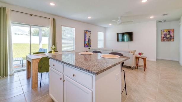A modern kitchen with a granite countertop, white cabinetry, and a dining area with a bench.