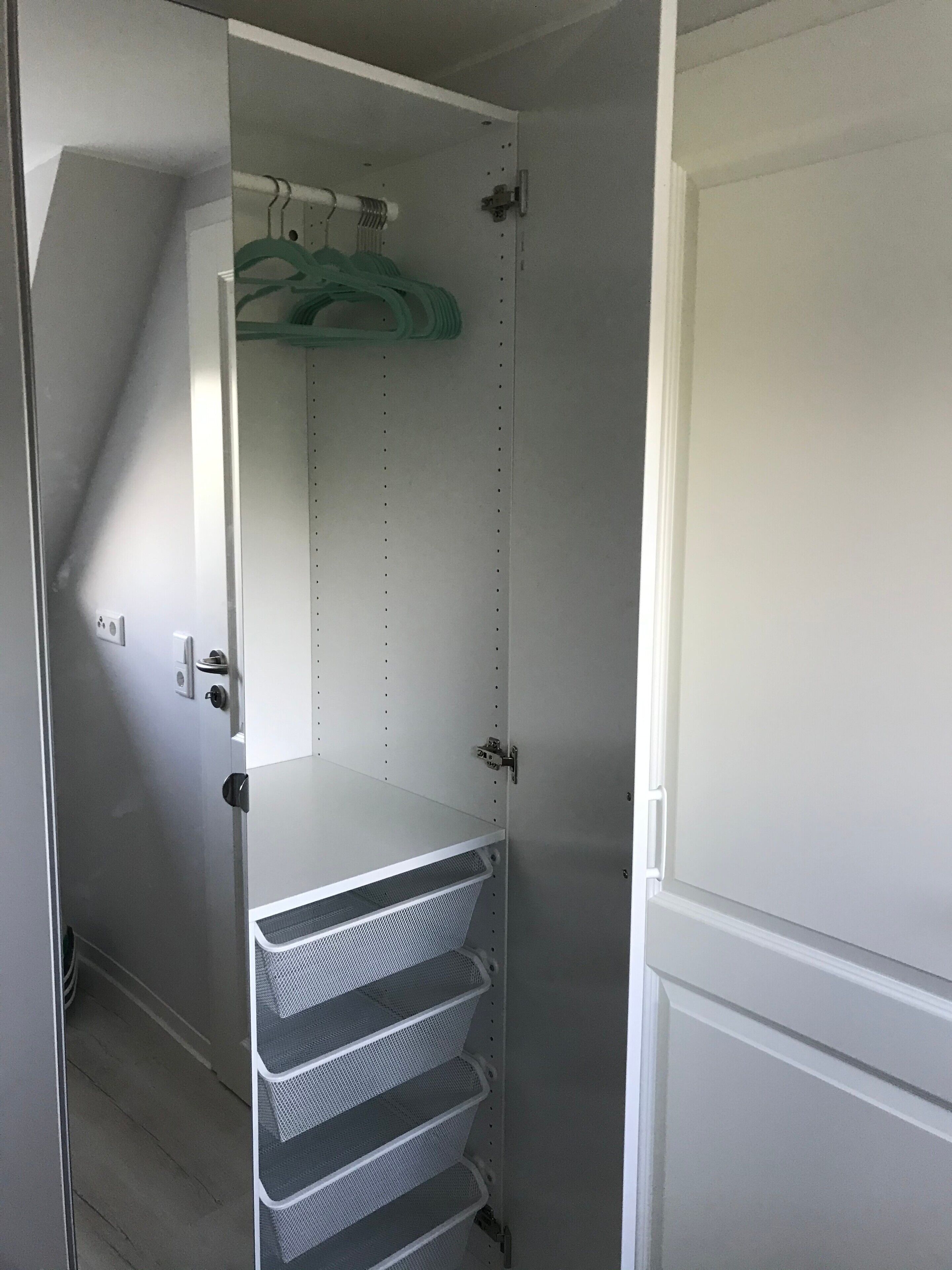 A walk-in closet with a white door, a metal shelving unit, and a hanging rod with clothes.