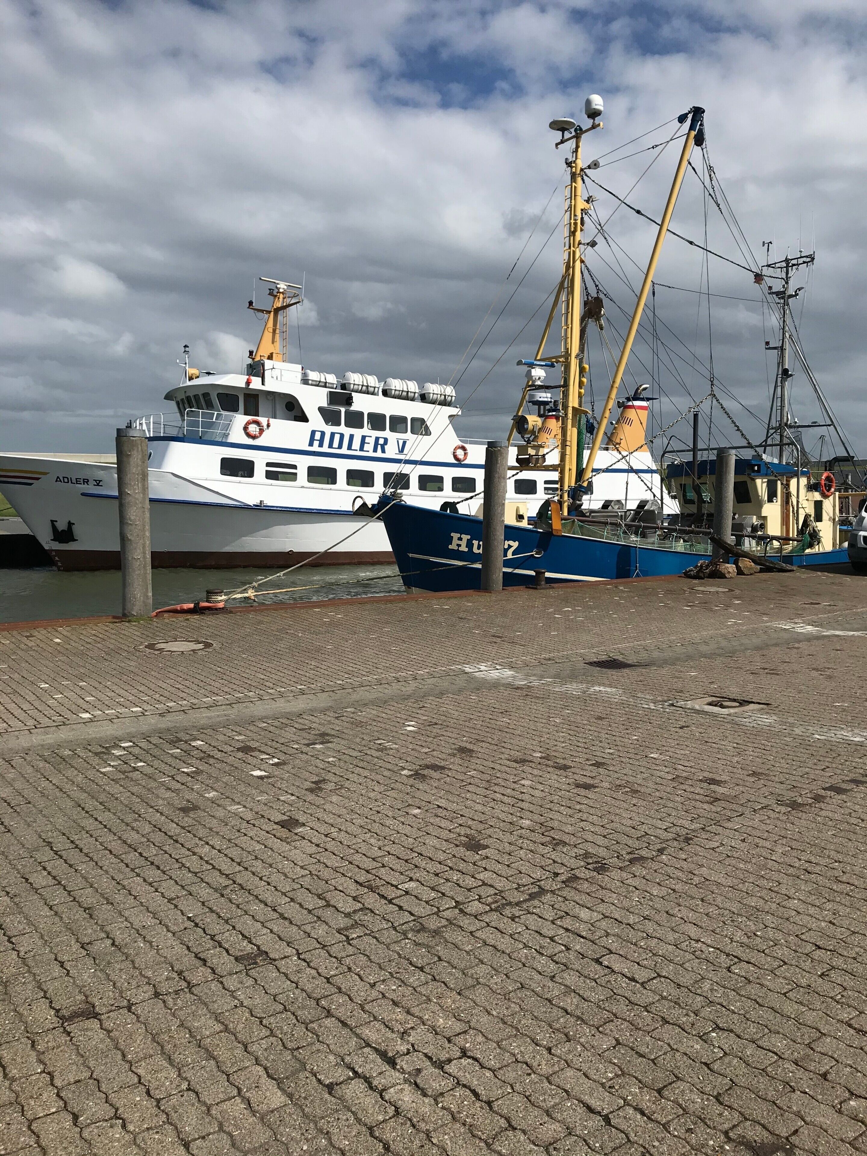 Een haven met een groot wit en blauw schip, genaamd 'HULFRY', afgemeerd aan een steiger.