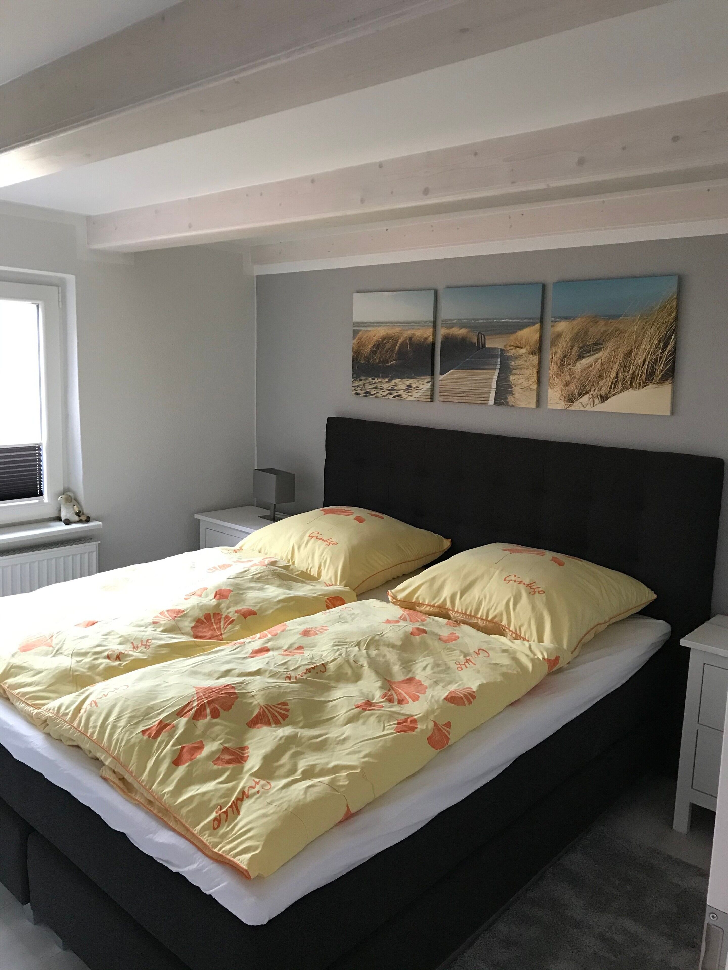 Een slaapkamer met een bed, nachtkastje, raam en een muur met drie ingelijste foto's.