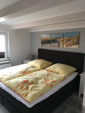 Ein Schlafzimmer mit einem Bett, einem Nachttisch, einem Fenster und einer Wand mit drei gerahmten Bildern.