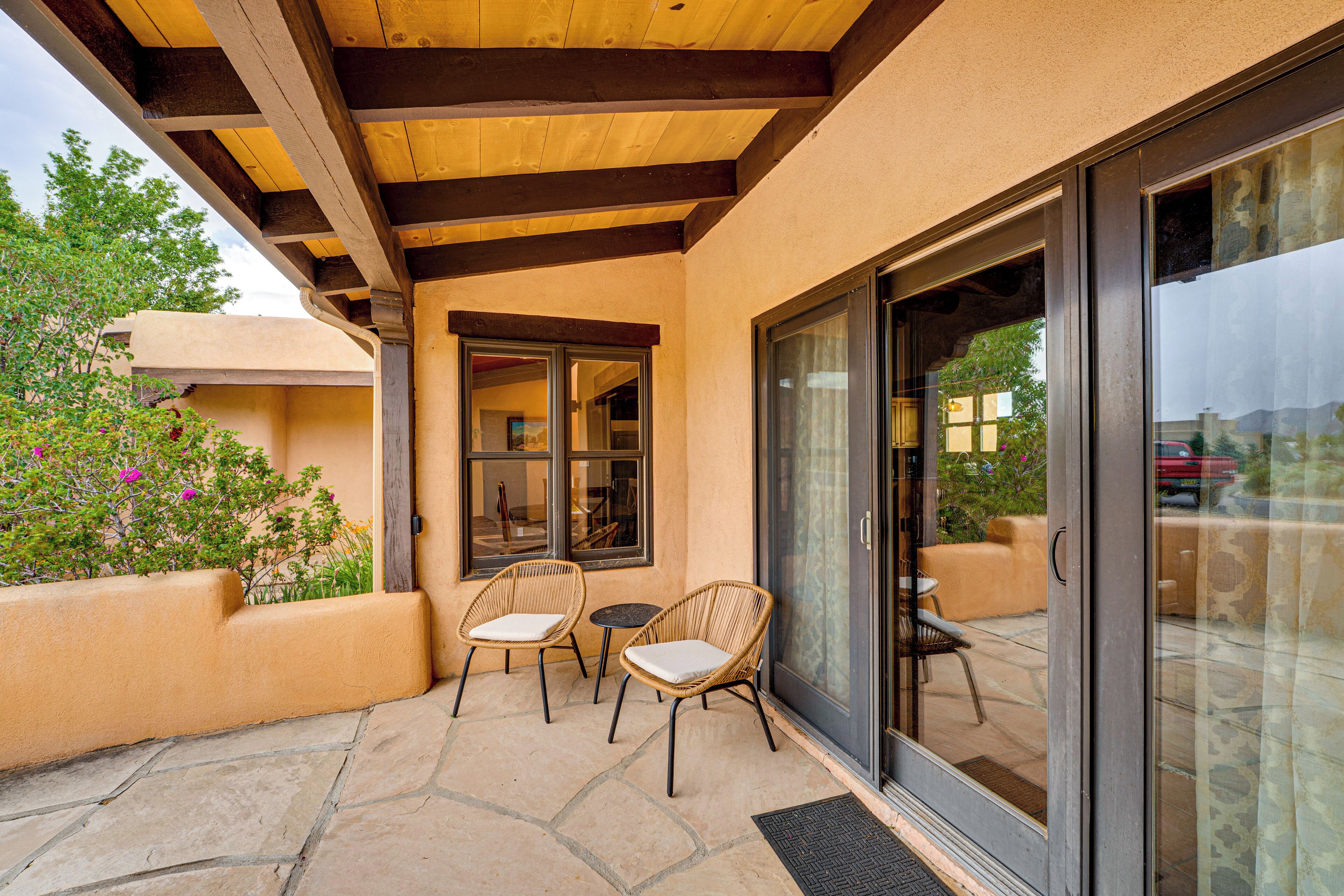 An outdoor patio with two wicker chairs and a small table, a wooden ceiling, and a glass door leading to a patio area.