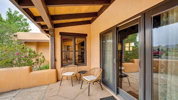 An outdoor patio with two wicker chairs and a small table, a wooden ceiling, and a glass door leading to a patio area.