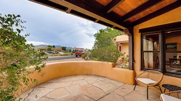 A patio with stone flooring, wicker chairs, and a view of the street and mountains.