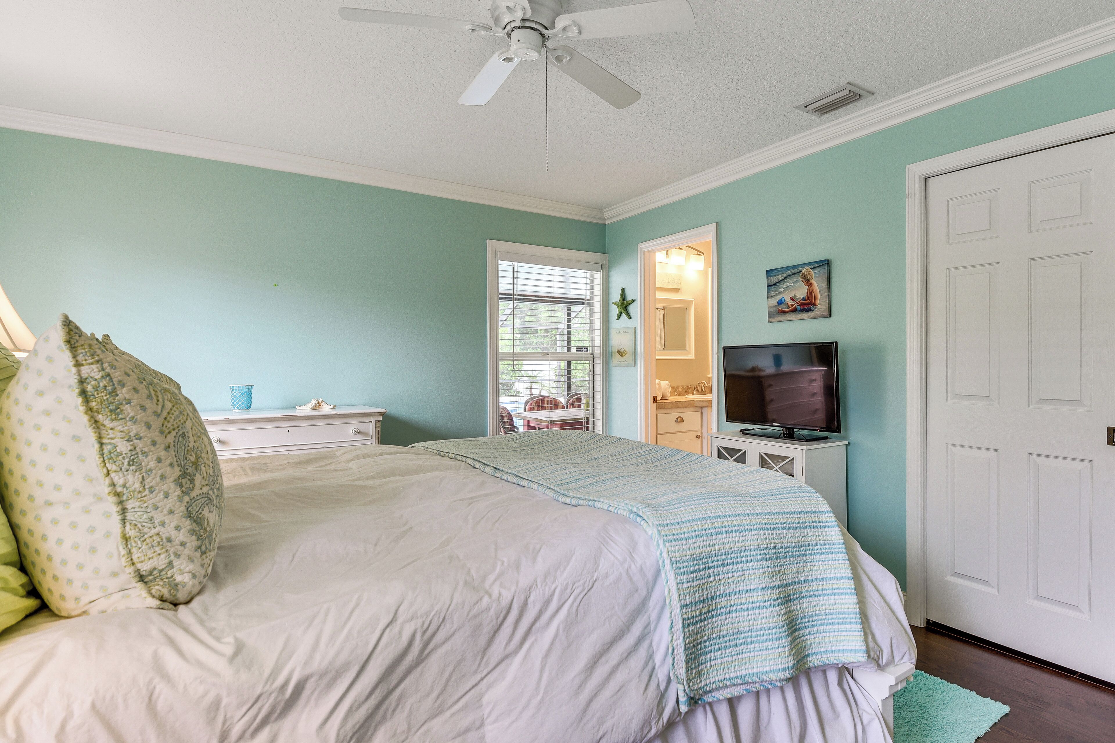 A bedroom with a bed, a ceiling fan, a television, and a door.