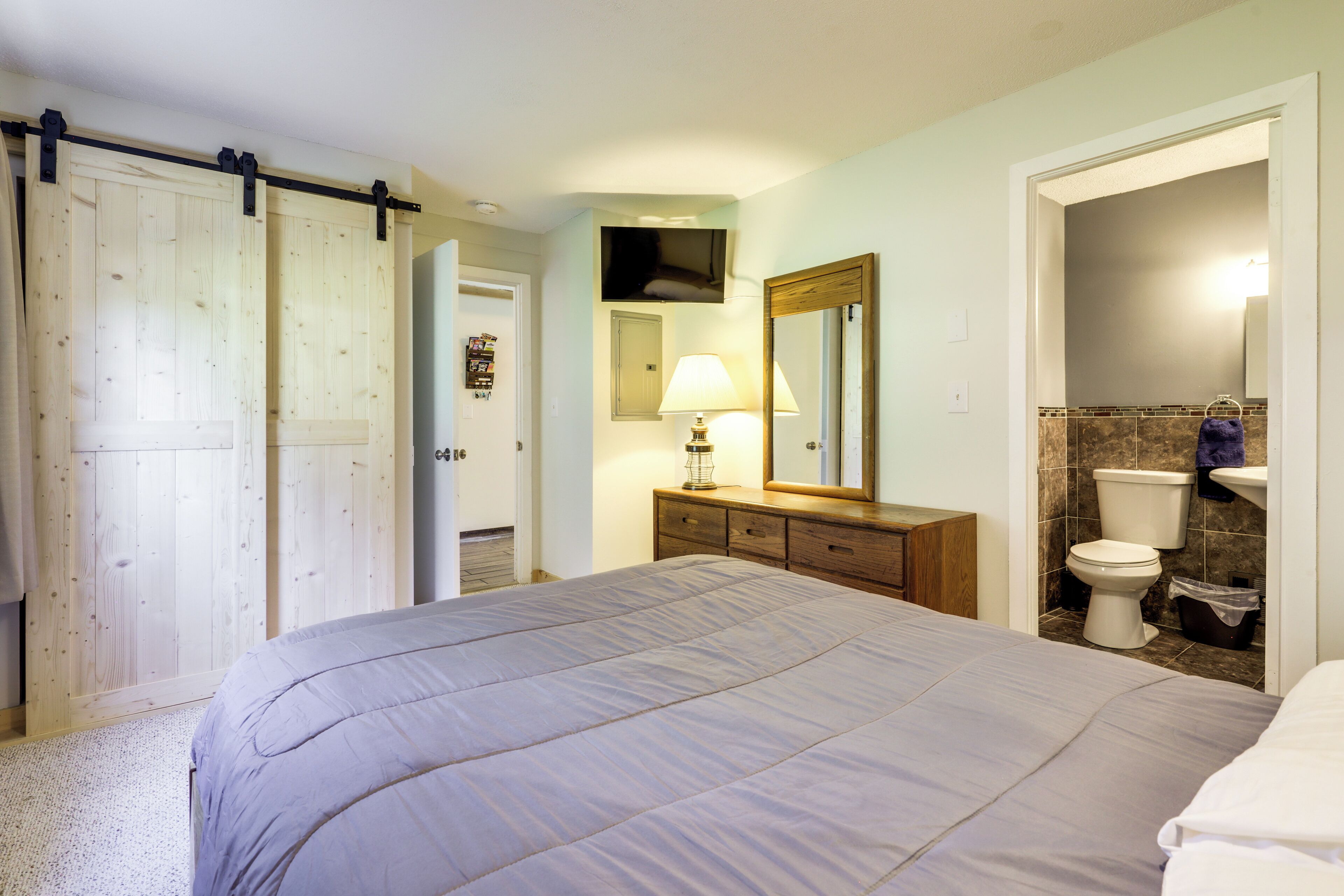 A bedroom with a bed, a dresser, a television, and a bathroom with a toilet and sink.