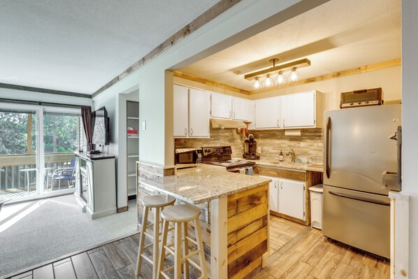 A modern kitchen with wooden accents, a large island with stools, and a built-in oven. - Walk to Weirs Beach! Family Escape w/ Balcony (Laconia)