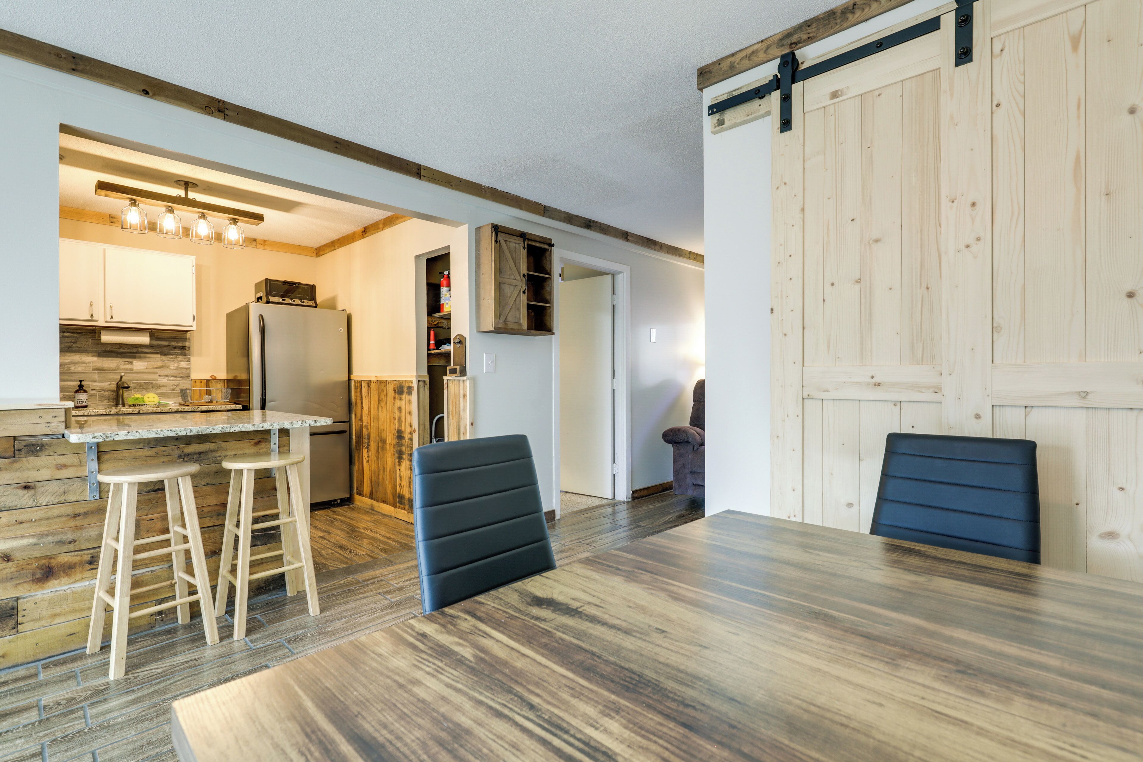 A modern kitchen with a built-in refrigerator, wooden bar stools, and a dining table with chairs.