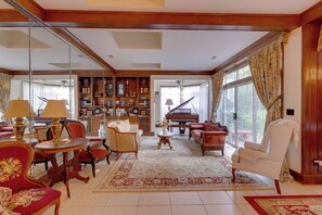 A spacious living room with a grand piano, a large bookshelf, and a red armchair.