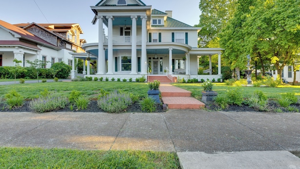 A large, two-story house with a prominent front porch, a symmetrical facade, and a well-maintained lawn.