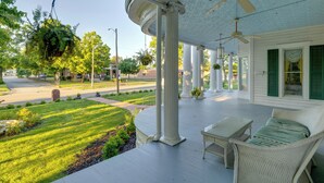 A porch with white wicker furniture, a hanging plant, and a ceiling fan.